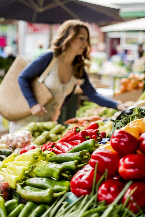 Gemüsestand auf einem Wochenmarkt. Frau im Hintergrund die einkauft.