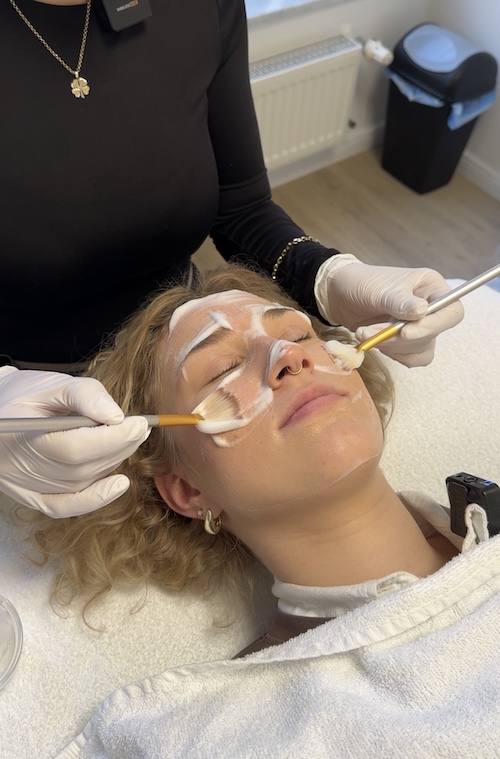 Lina liegt auf der Behandlungsliege und hat Schaum im Gesicht. Zwei Pinsel verteilen den Schaum im ganzen Gesicht.