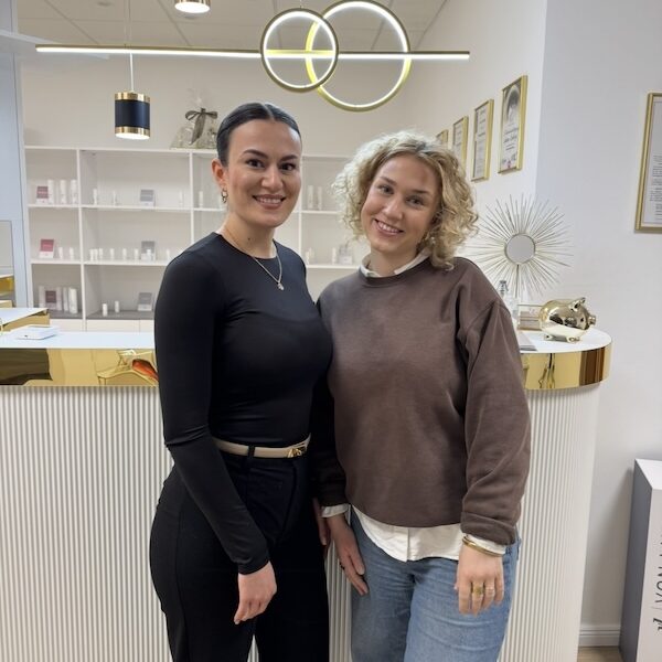 Luana und Lina machen ein Foto im Kosmetikstudio Main Beauty. Sie lächeln in die Kamera und stehen vor der Rezeption.