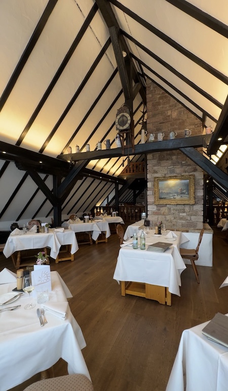 Gedeckte Tische im Essbereich der Neumühle mit hohen Decken und einem Kamin in der Mitte.