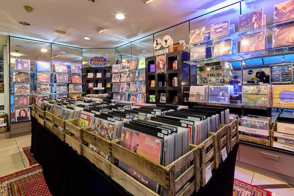 Blick in den Ausstellungsraum der Plattentruhe: Holzkisten gefüllt mit Platten im Vordergrund. Im Hintergrund Regale gefüllt mit Platten.