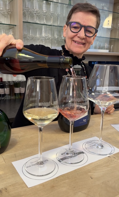 Inhaberin von Weingut Lange schenkt lächelnd Wein in ein Weinglas ein.