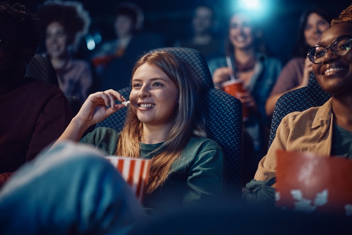 Frau sitzt lächelnd im Kino und isst Popcorn.