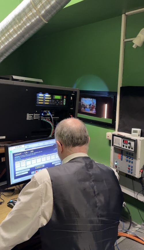 Der Kinobetreiber sitzt vor dem Computer und im Hintergrund sieht man den digitalen Projektor, der das Bild auf die Leinwand wirft.