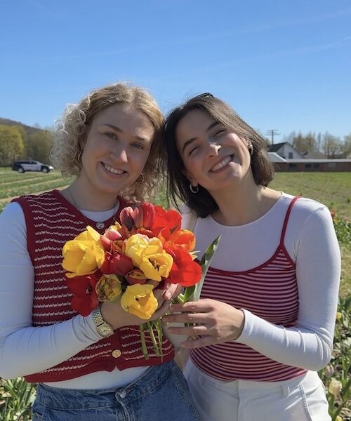 Zwei junge Frau halten lächelnd einen Blumenstrauss in die Kamera.